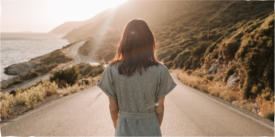 žena stojí na cestě a pžed sebou má rozsáhlou krajinu.
